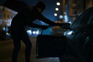 Ladro cerca di forzare la portiera di un’auto in un parcheggio.